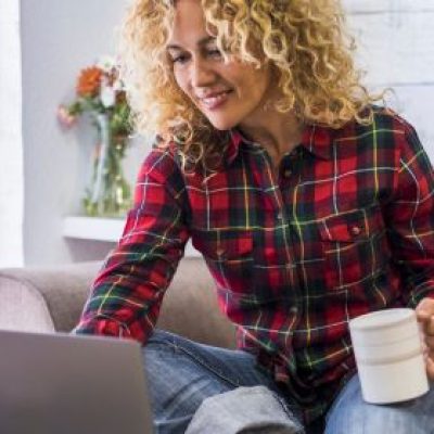 A woman sitting on a couch with her laptop holding her coffee.