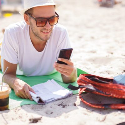 A man banking with his phone on the beach.
