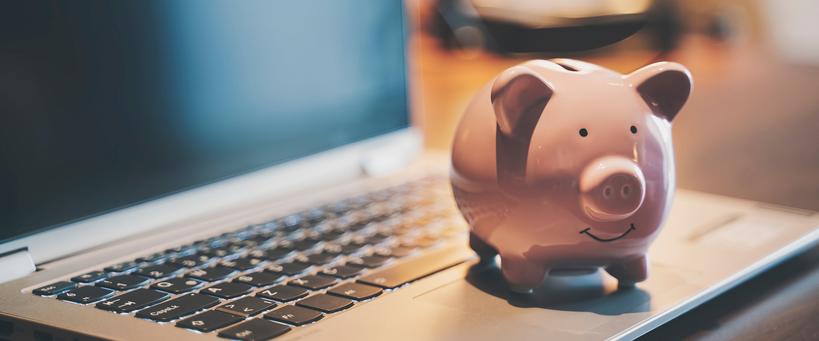 A happy pink piggy bank sitting on a laptop.