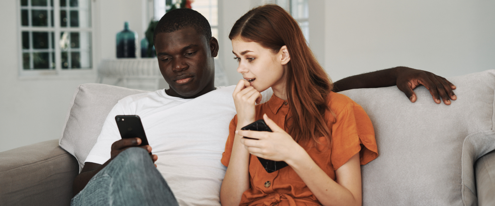 A man holds his phone while his girlfriend looks at it with intrigue.
