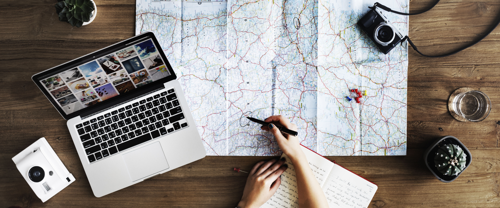 A person uses a map, notebook and laptop to plan a trip.