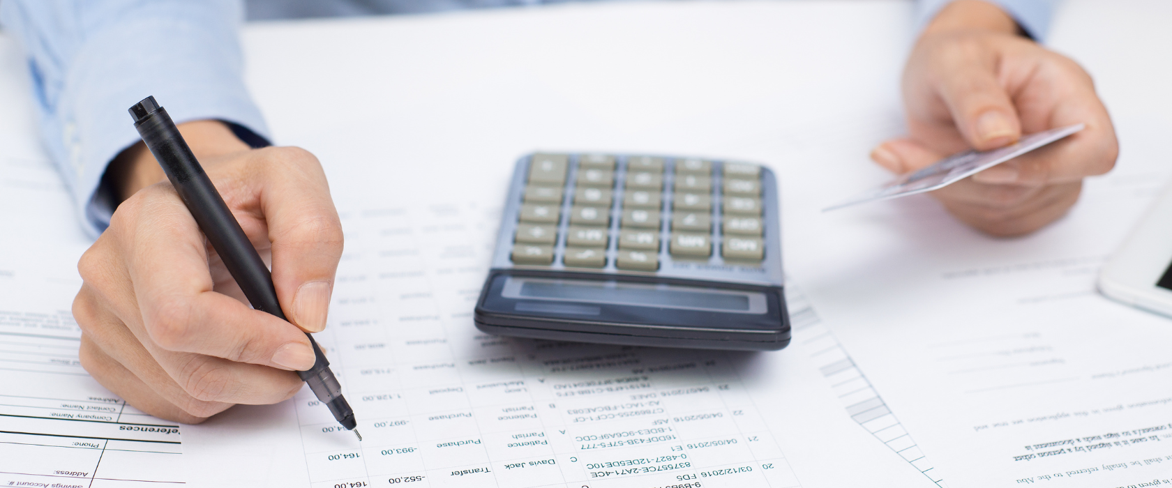 A man holding a credit or debit card using a calculator and a pen to check a bank statement.