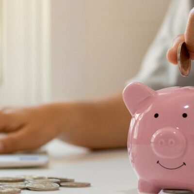 person putting coins into a pink piggy bank.